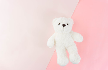 The cute white fluffy teddy bear lay on two tone of pink background in top view.