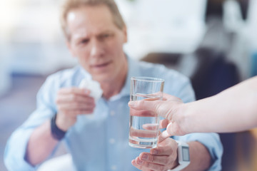 Take it. Selective focus of glass with water being given to the nice upset handsome man