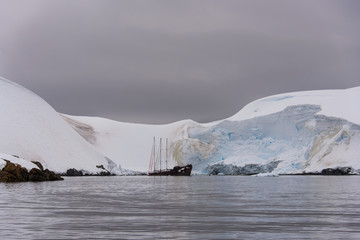 Two sailing yachts in the antarctic sea moored to rusty wreck