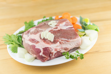 Pork butt with vegetables, herbs and garlic on a white plate, wooden background