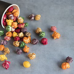 Multicolored popcorn and black paper cup on gray background.