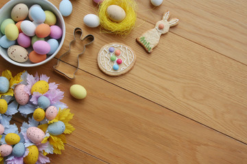 Easter background. Multicolored choccolate eggs, cookies in shape of bunny, bell and egg,and decoration on wooden table
