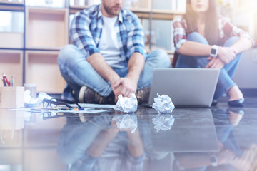 Obraz premium Casual lifestyle. Attentive man bowing head while looking at laptop and sitting on the floor near his colleague