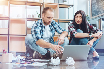 Obraz premium Need your advice. Attractive brunette woman keeping smile on her face and sitting on the floor while listening to her colleague