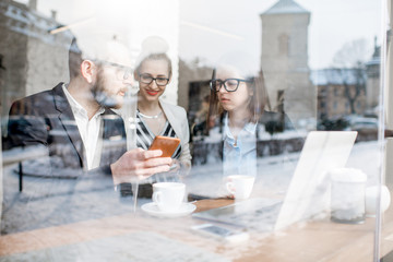 Business people during the coffee break sitting with laptops near the window. View through the window with city reflection