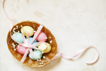 Traditional easter card template with pastel colors painted organic eggs in wicker basket with hay and decorative wildflowers.
