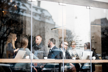 Business people during the coffee break sitting with laptops near the window. View through the window with city reflection