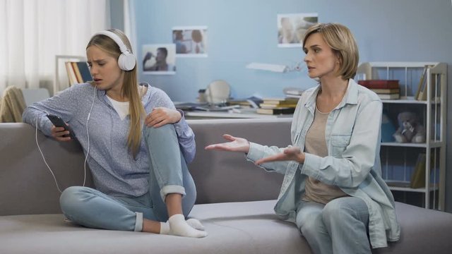 Girl in music headphones showing stop gesture to shouting mother, generation gap