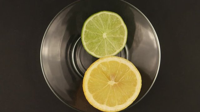 Lime and lemon in a section on a glass plate on a black background