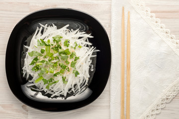 On a black plate chinese salad of raw radish daikon, parsley, green onion, sesame and  with the addition of soy sauce. A vegetarian dish, healthy food. Top view, copy space.