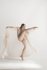 Fototapeta na wymiar Young beautiful dancer in beige swimsuit dancing on gray background