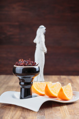 shisha with Apple flavor in a glossy black bowl, cooked for Smoking, stands on a tray with three juicy slices of orange
