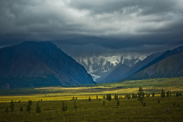Beautifull  view to snow mountains and green field with sunlight and sky in the storm
