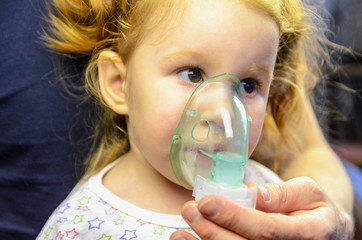 Little girl having a medical inhalation treatment with a nebulizer at home.