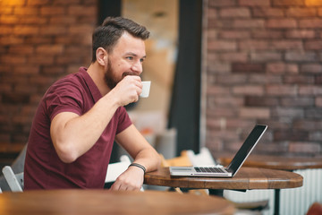 Man drinking coffee and using laptop while sitting in cafeteria.