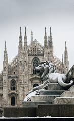 Fototapeta premium Falling snowflakes at ornate of lion on Piazza del Duomo in Milan, Lombardy, Italy. The Patron Saint of Milan, Madonnina, is visible above the Duomo Cathedral, with copy space
