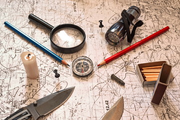 candle, open box of matches, loupe, folding knife and blade, bullet, flashlight, red and blue pencil, pin and compass on vintage military topographic map