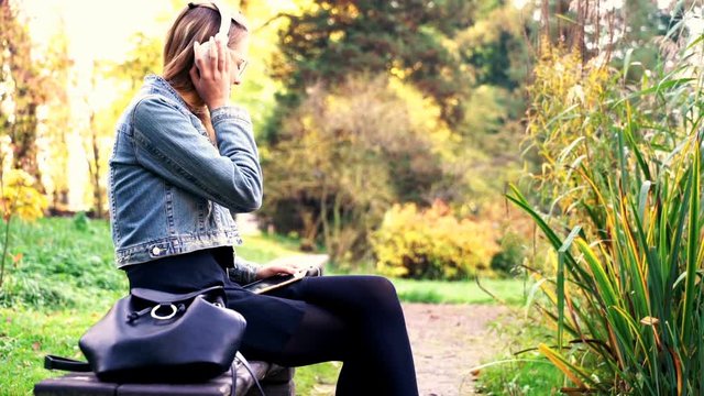 Pretty woman listen to music while sitting on the bench in beautiful garden
