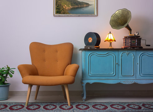 Vintage interior of retro orange armchair, vintage wooden light blue sideboard, old phonograph (gramophone), vinyl records and illuminated table lamp