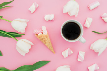 Tulips flowers with mug of coffee, marshmallows and waffle cone on pastel pink background. Blogger concept. Flat lay, top view.