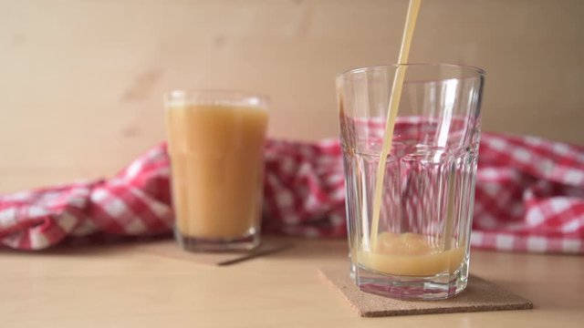 Pouring peach juice into a drinking glass on kitchen table, flat ungraded footage