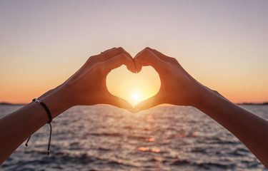 Hands in the shape of a heart at sunset and against the background of the sea.