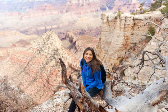 Travel hiking photo of young beautiful woman with backpack at Grand Canyon viewpoint, Arizona, USAm smiling at camera.