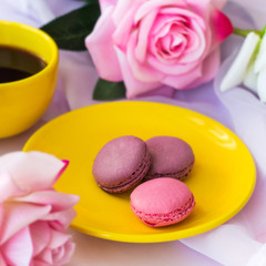 yellow hot drink cup  and macaroons on a plate and  blurred roses on a table