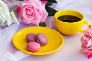 yellow hot drink cup  and macaroons on a plate and  blurred roses on a table