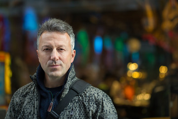 Handsome middle-aged man walking autumn evening street and posing over showcase. Urban male portrait, image toned and noise added, soft focus.