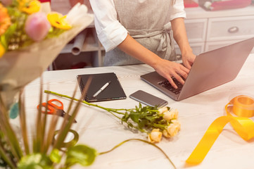 Female florist receiving an order on laptop, making notes in notebook. Woman works in his own flower shop.