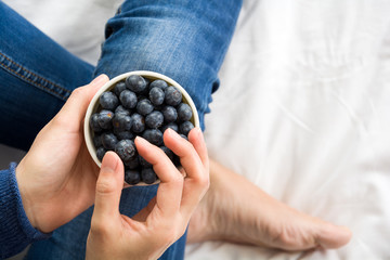 Healthy eating concept. Woman having blueberries in bed. Top view.