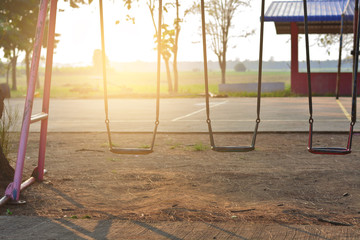three empty swings in a playground with a bright sun shining in the background.