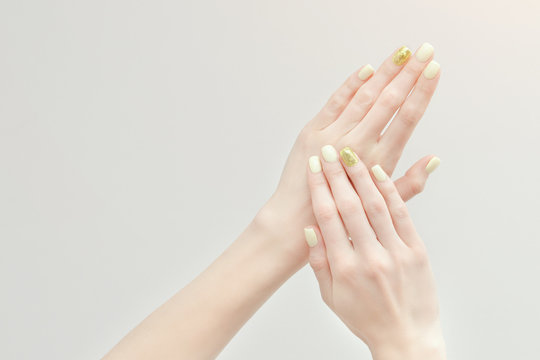 Beautiful female hands with a manicure on a light background. Yellow with gold nails