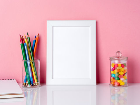 Blank white frame and crayon in jar, candys on a white table against the pink wall with copy space