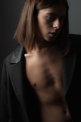 Feminine young man with coat on a dark background. Close up