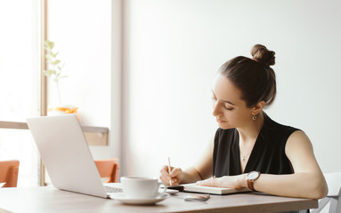 Beautiful girl working out a plan of the project and concept. Girl paints a website design on a laptop. student prints a message on the phone in the messenger. Development. Digital marketing