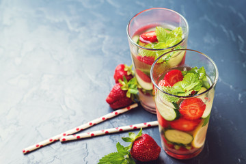 Detox water with strawberry and cucumber in two glasses on dark background. Copyspace.