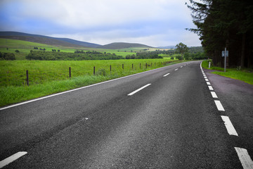 Asphalt road through the green field and clouds on blue sky