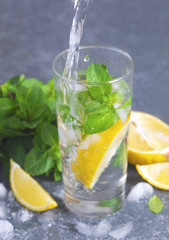 Glass of aced water with lemon and mint. Water drink pouring into glass