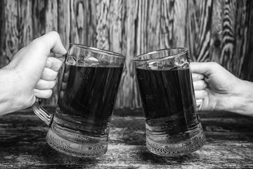 Two mug of green beer in in hands against a wooden wall. Black and white photo.