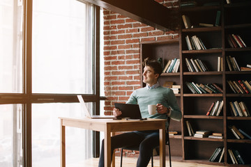 Young handsome guy is going  to enter university and prepares for exams in different fields with the help of his laptop and books in the library. Student planning his lessons at the university.