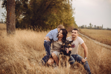 portrait of a young family who plays with a dog on nature in the autumn afternoon