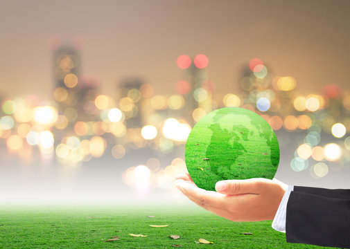 World environment day concept: Businessman hand holding earth globe of grass over blurred city background