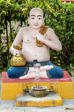 A statue of a man sitting with a bag of money at Buddhist monastery - Reclining Buddha Wat Chaiyamangalaram, Penang, Malaysia.