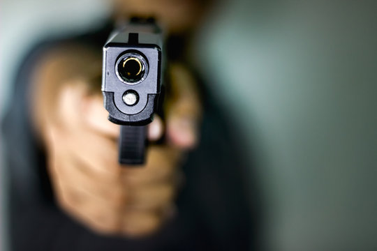 A man holding a gun pointing to a target demonstrates the violence of a gun with blurry background