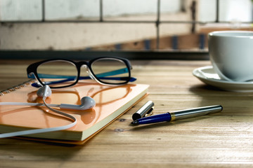 Top view of the desk with notebooks pens glasses headphones and alarm clocks on the table.
