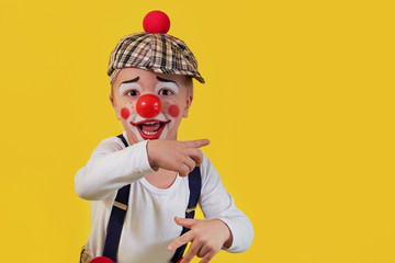 Child clown smile shows a finger copy space area on yellow background. Funny little clown with red...