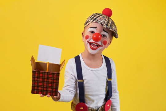 Funny Kid Clown Isolated On Yellow Background. Beautiful Playful Portrait Child Boy Jester In Makeup. Expression Face Joy, Smile, Fun, Cheerful. 1 April Fool's Day Concept.