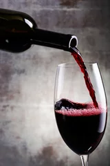 Fotobehang Pouring red wine into the glass against wooden background © alefat